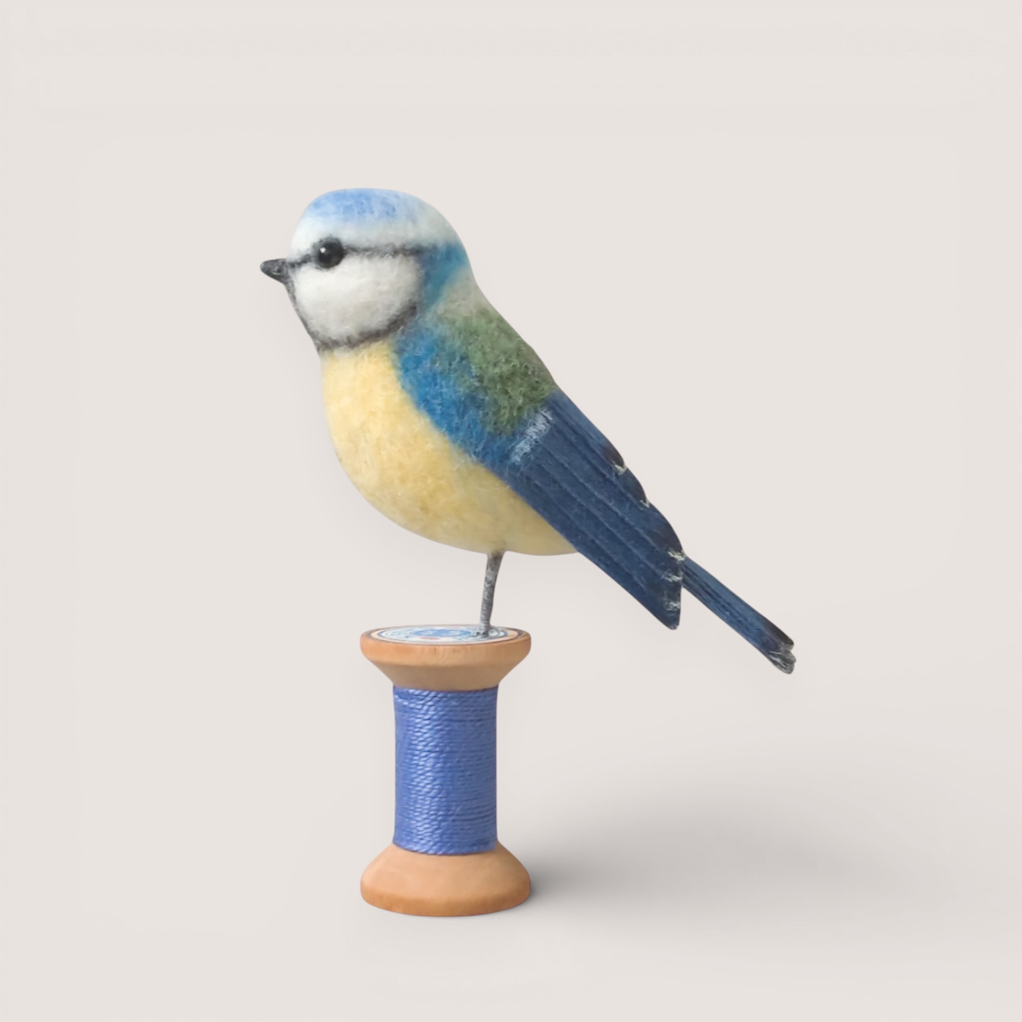 Handmade needle-felted blue tit sculpture on a wooden bobbin by Grey Wren Studio.
